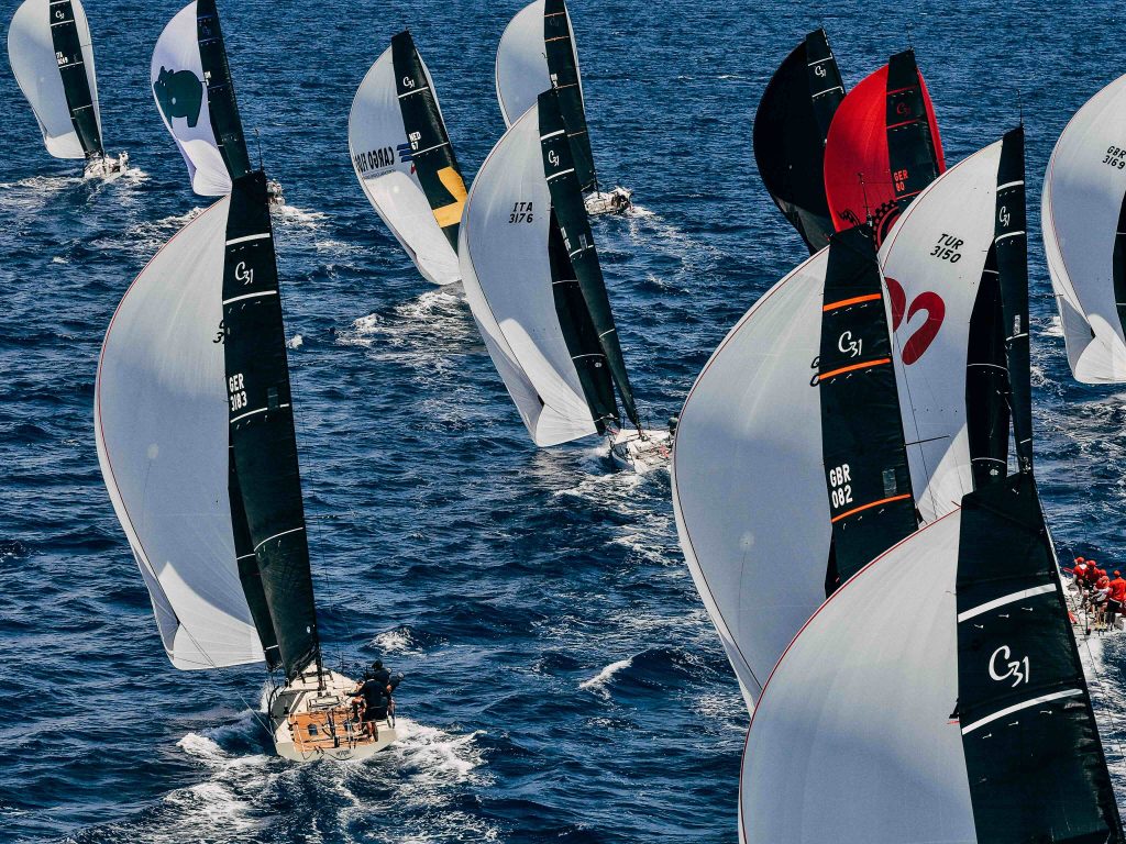 A dense fleet of Cape 31 one-design yachts racing under spinnaker, sails marked C31, including boats from Germany, Italy, Great Britain and Türkiye